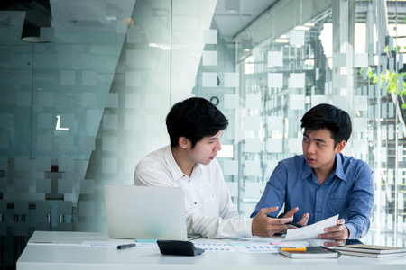 Young Asian business men meeting and discuss work project at office desk. Business professional teamwork coworkers discussing information document at table. Business corporate partnership concept.の写真素材