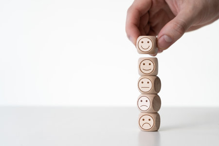 Business man hand putting stack of wooden dice cubes with smile icon emoji on white table background. Customer satisfaction survey, user experience feedback, and rating concept.の写真素材