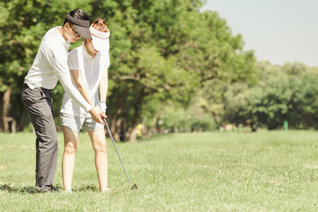 Asian couple playing golf. man teaching woman to play golf while standing on fieldの写真素材