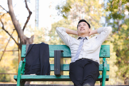 Portrait asian business man sit on a green wooden chair relaxation in parkの写真素材