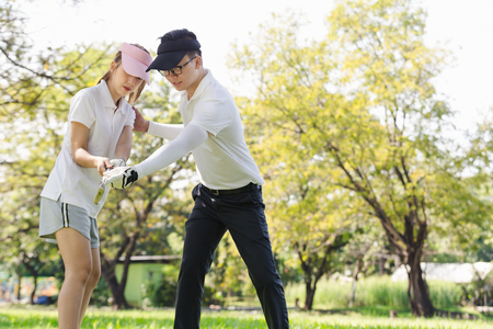 Asian couple playing golf. man teaching woman to play golf while standing on fieldの写真素材