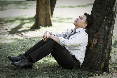 Asian business man failing and serious under tree in the parkの写真素材
