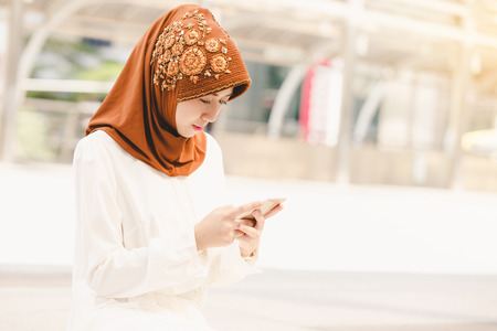Portrait of a happy young Muslim woman using mobile phone in the cityの写真素材