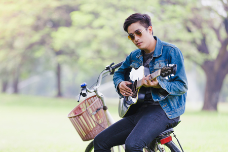 Portrait asian young men sitting on bicycle play guitarの写真素材