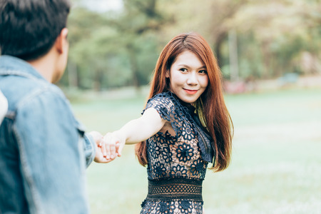 Asian couple lovers hold one's hands under a vast field of nature in a park.の写真素材