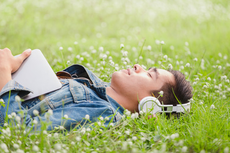 Asian young men lie about on nature listen to music with headphoneの写真素材