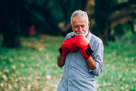 Senior man prepared for a fight with red boxing gloves in nature backgroundの写真素材