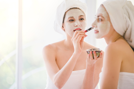 Beautiful young woman and friend spa applying cosmetic mask cream on face relaxing receiving massage,Spa face conceptの写真素材