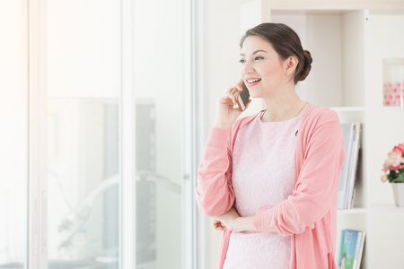 Business woman standing working near a window and holding call talking by phone at office.の写真素材