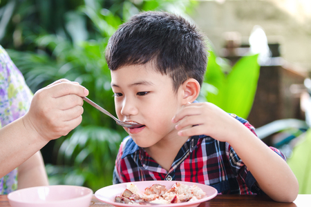 Asian little boy eating with rice food on the wooden table,Mother feeding rice foodの写真素材