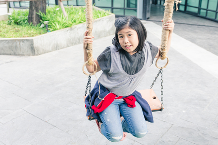 Asian girl sitting on chain swing woodの写真素材