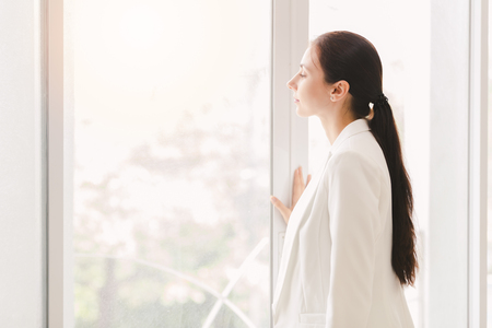 Business women wearing white suit standing looking out windowの写真素材