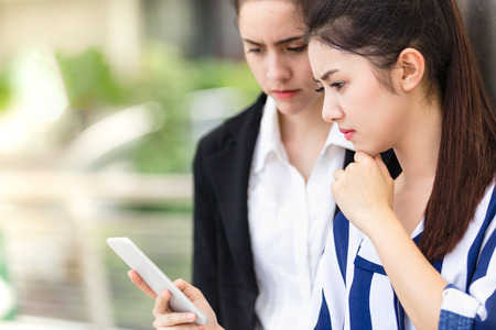 Two Asian women who hold a smartphone read the message seriouslyの写真素材