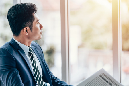 Asian businessman sitting reading newspaper in office smile on faceの写真素材