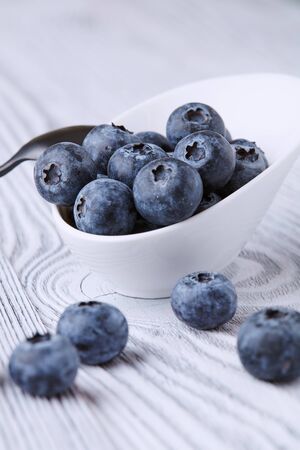 Ripe and sweet blueberries on a textured wooden table in a beautiful white ceramic Cupの写真素材