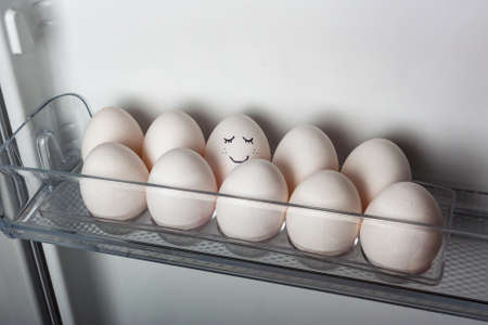 smiling egg in a row of white eggs in fridgeの写真素材