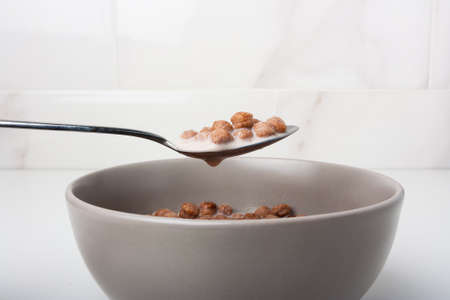Breakfast crunchy chocolate balls with milk in a spoon on white background