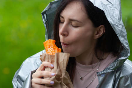 Young woman in raincoat eating burrito outdoorの写真素材