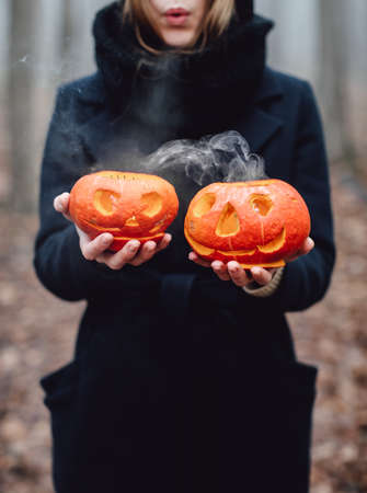 A creepy witch holds a steaming pumpkin in a deep forest. Dark trees in foggy forest. Halloween...