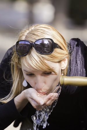 Young lady drinking tap water from the fountain in the city park on a hot summer day.の写真素材