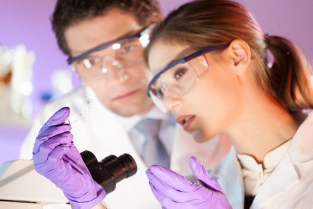 Attractive young scientist and her post doctoral supervisor looking at the microscope slide in the forensic laboratory.の写真素材