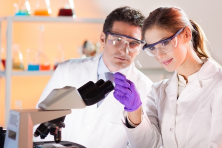 Attractive young scientist and her suprvisor looking at the microscope slide in the forensic laboratory.の写真素材