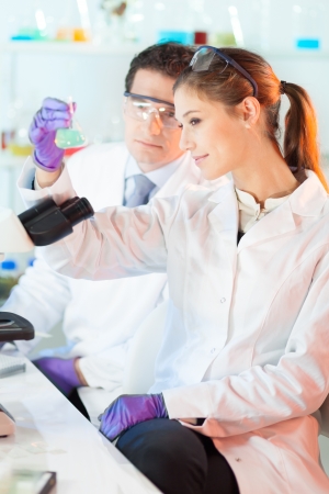 Chemical laboratory scene: attractive young student and her post doctoral supervisor scientist observing the green indicator solution color shift in glass flask.の写真素材