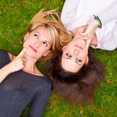 Two beautiful girls lying in the grass and laughing.の写真素材