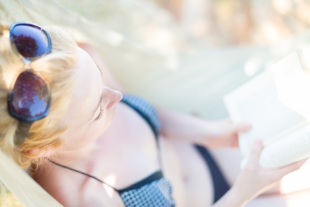 Beautiful girl lies on hammock on the beach and reads the book の写真素材