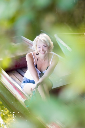Relaxed young blonde woman  enjoying the sunny summer day on a vintage wooden boats on a lake in pure natural environment on the countryside.の写真素材