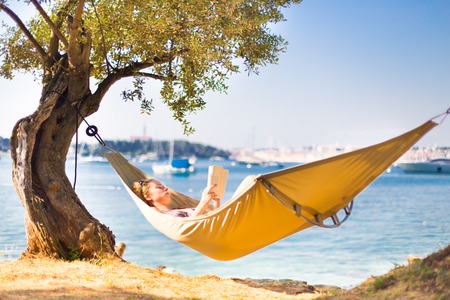 Beautiful girl lies on hammock on the beach reading book.の写真素材