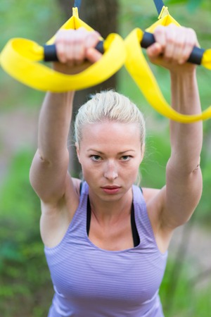 Young attractive woman does suspension training with fitness straps outdoors in the nature.の写真素材