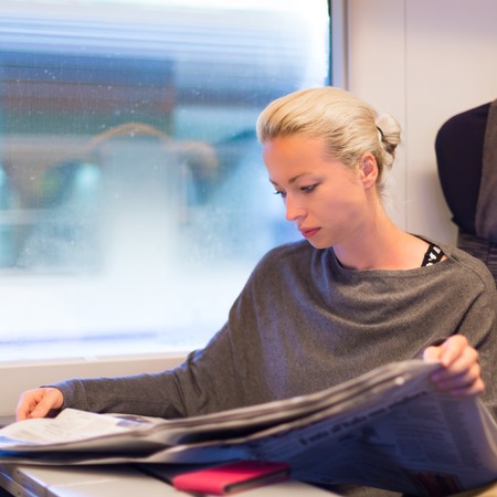 Thoughtful young lady reading while traveling by train の写真素材