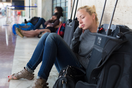 Tired female traveler waiting for departure, resting on the station floor with all her luggage の写真素材