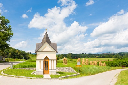 Bela krajina, Slovenia  Traditional christian chapel and hay stacks on the field in the background の写真素材