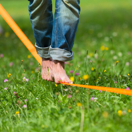 Guy practising slack line in the city park. Slacklining is a practice in balance that typically uses...