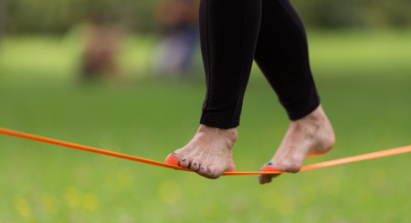 Lady practising slack line in the city park. Slacklining is a practice in balance that typically uses nylon or polyester webbing tensioned between two anchor points.の写真素材