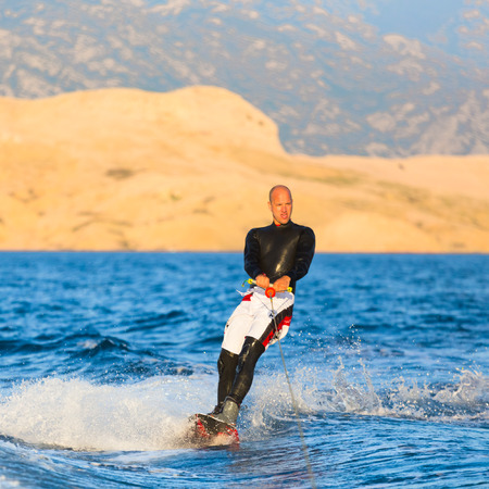 Wakeboarder in wetsuit riding in sunset. Wakeboarding is a surface water sport which involves riding a wakeboard over the surface of a body of water.の写真素材