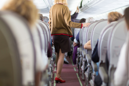 Interior of airplane with passengers on seats and stewardess walking the aisle.の写真素材