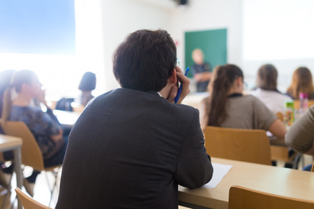 Teacher at university in front of a whiteboard screen. Students listening to lecture and making notes.の写真素材