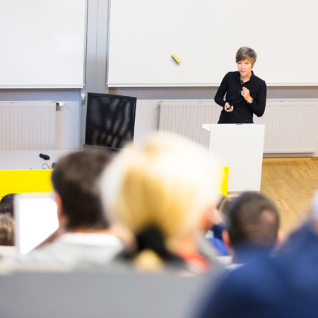 Speaker giving presentation in lecture hall at university. Participants listening to lecture and making notes.の写真素材