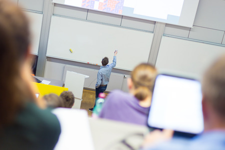 Students listening to lecture and making notes. Professor giving presentation in lecture hall at...