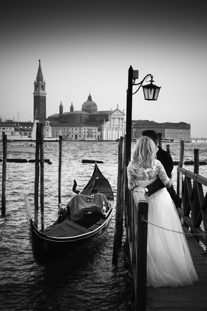 Romantic married couple in Romantic Italian city of Venice in black and white. Traditional Venetian wooden gondola and Roman Catholic church of San Giorgio Maggiore in the background.の写真素材