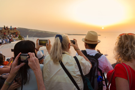 Large group of tourist watching and taking photos of famous sunset view in Oia village on Santorini island in Greece, Mediterranean Europe.の写真素材