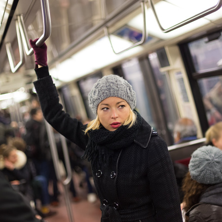 Beautiful blonde caucasian lady wearing winter coat traveling by metro in rush hour. Public transport.の写真素材