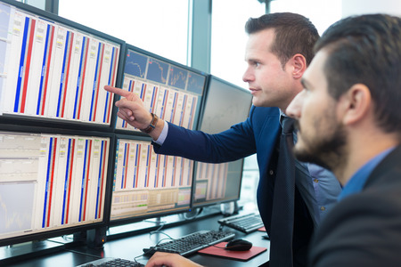 Stock traders looking at graphs, indexes and numbers on multiple computer screens