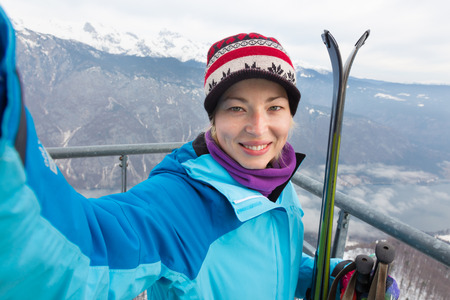 Cheerful lady taking selfie enjoing the snowy mountain view, excited before skiing.の写真素材