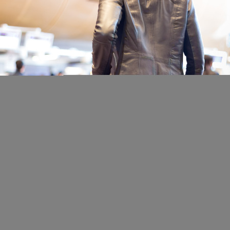 Casually dressed young stylish female traveller walking the airport terminal hall   draging suitcase and a handbag behind her. Blured background. Can also be used as railway, metro, bus station.の写真素材