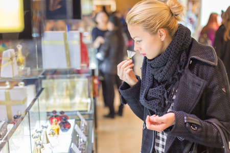 Beautiful blond lady testing and smelling perfume in a beauty store. Woman buying cosmetics in...