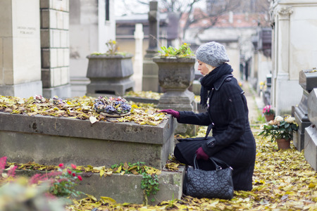 Solitary woman mourning with her hand on headstone, remembering dead relatives in on Pere Lachaise...